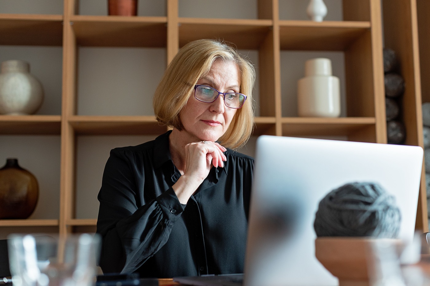 An older woman wearing glasses uses a laptop at a table at home.