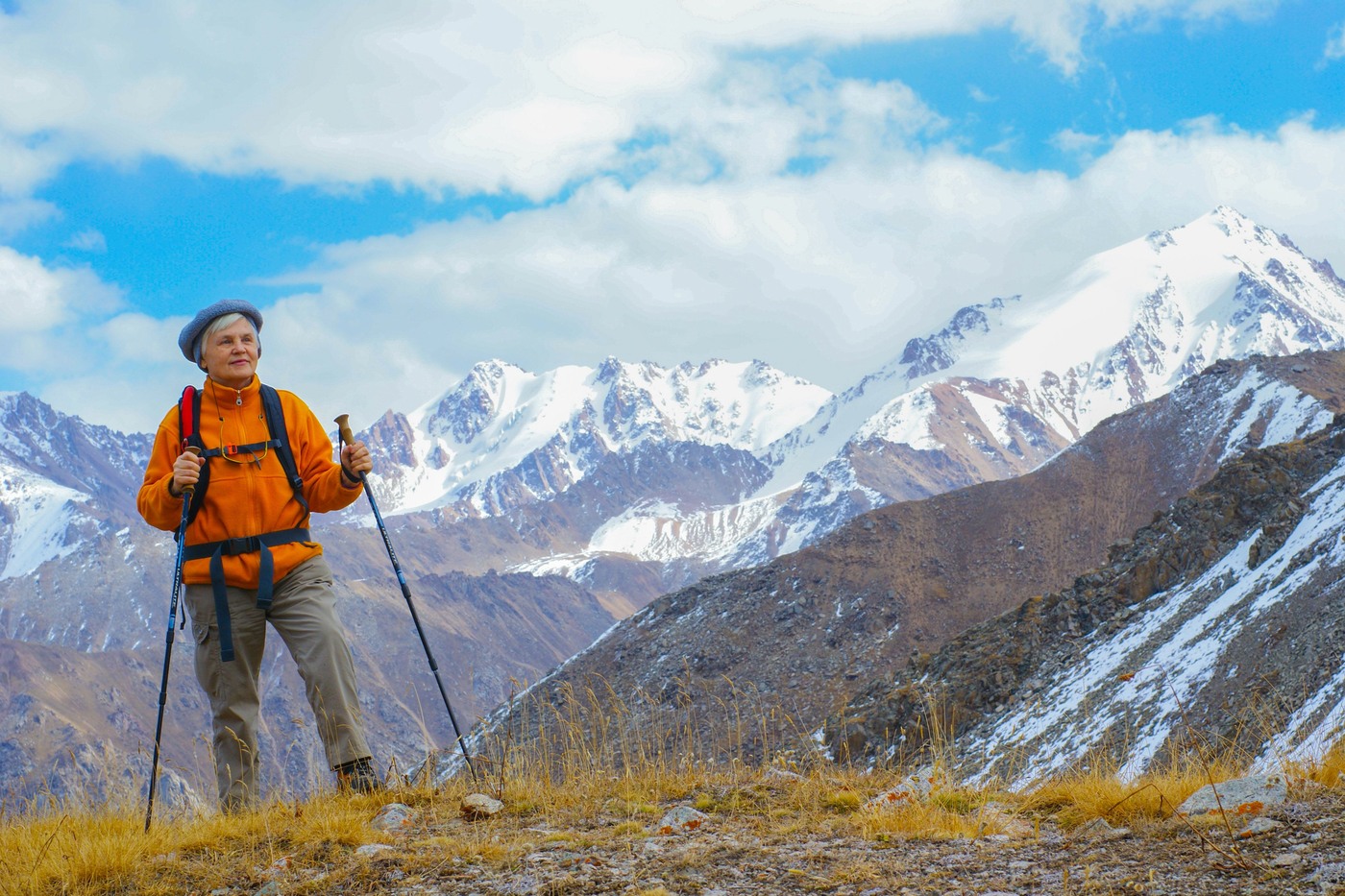 An older woman with a backpack and walking poles enjoys a mountain landscape.